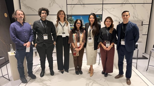 Group photo of eight architecture and design professionals standing together at an industry event, with a marble-textured backdrop and presentation screen behind them.