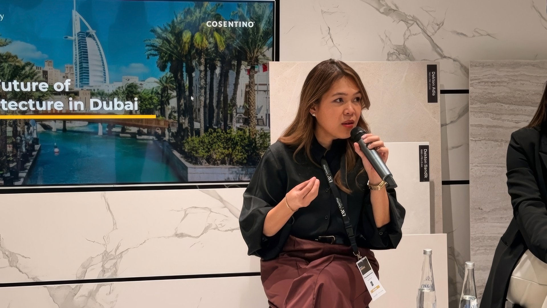Female speaker holding a microphone during a panel discussion on "The Future of Architecture in Dubai," with a screen displaying Burj Al Arab and Cosentino branding in the background.